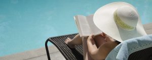 A woman reading a book by a pool.