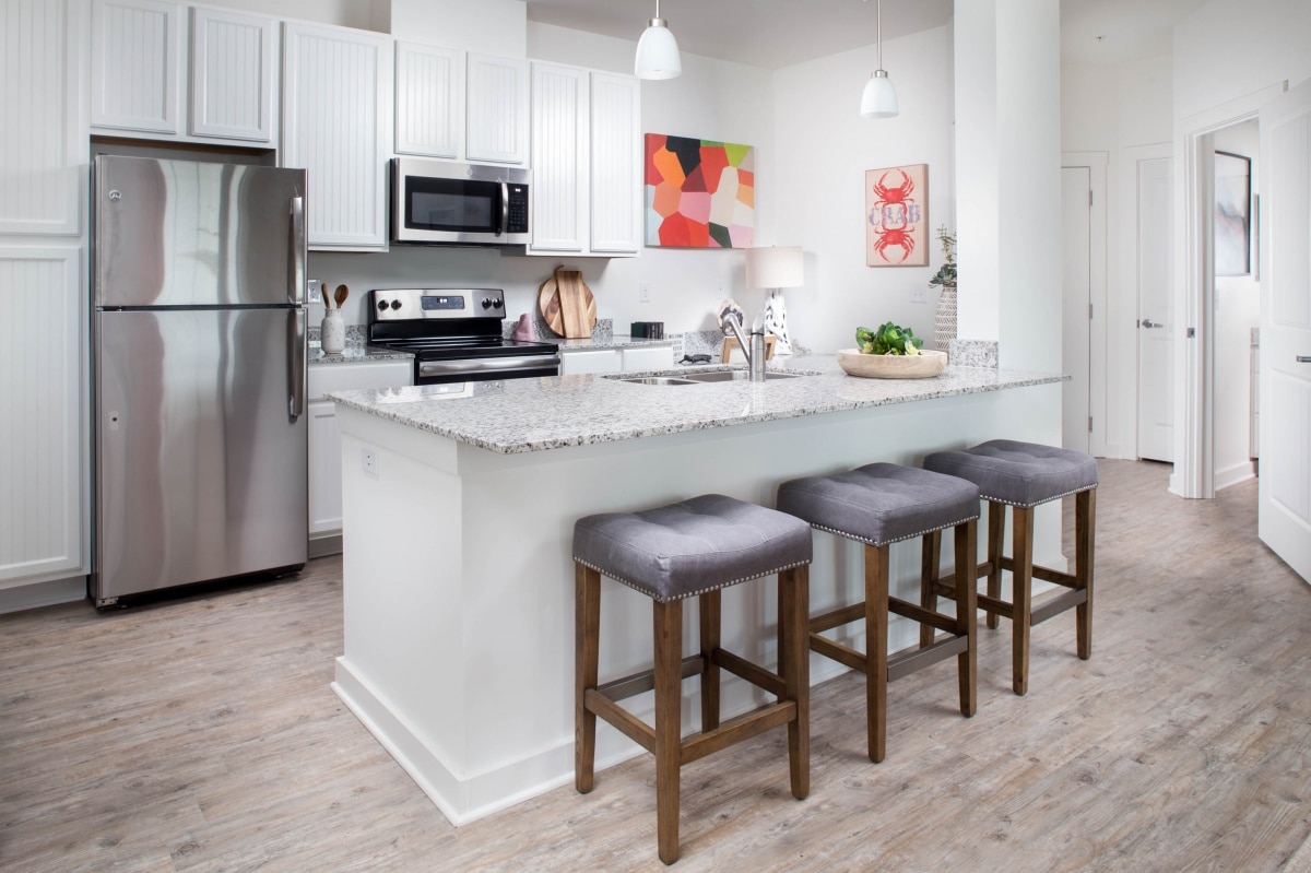 An apartment kitchen with stainless steel appliances and bar stools.