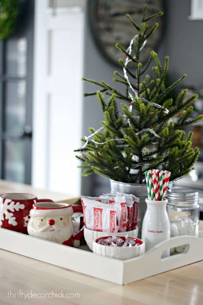 In an apartment kitchen, there is a tray adorned with a small tree and mugs.