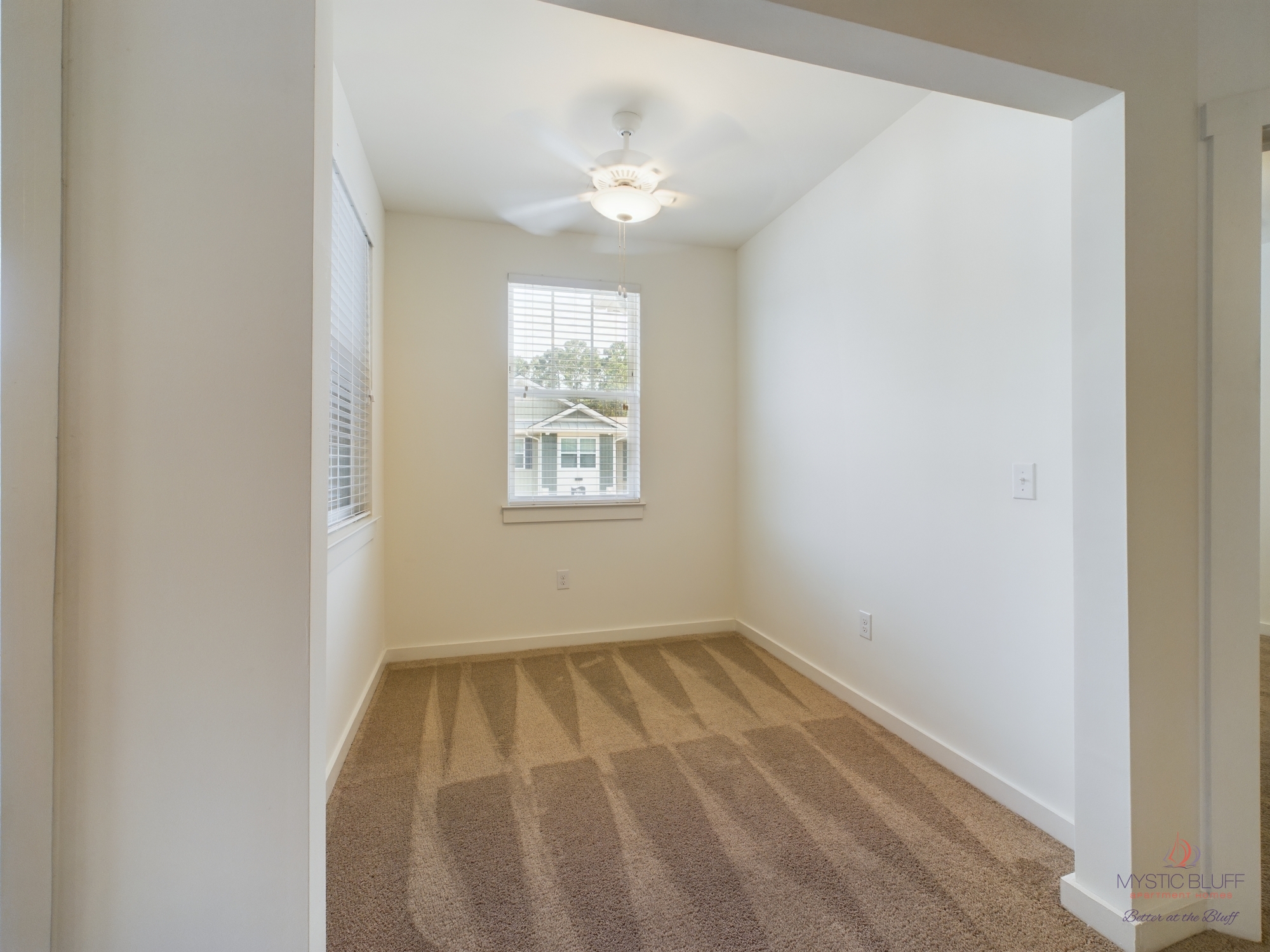 An empty apartment with a ceiling fan and carpet.