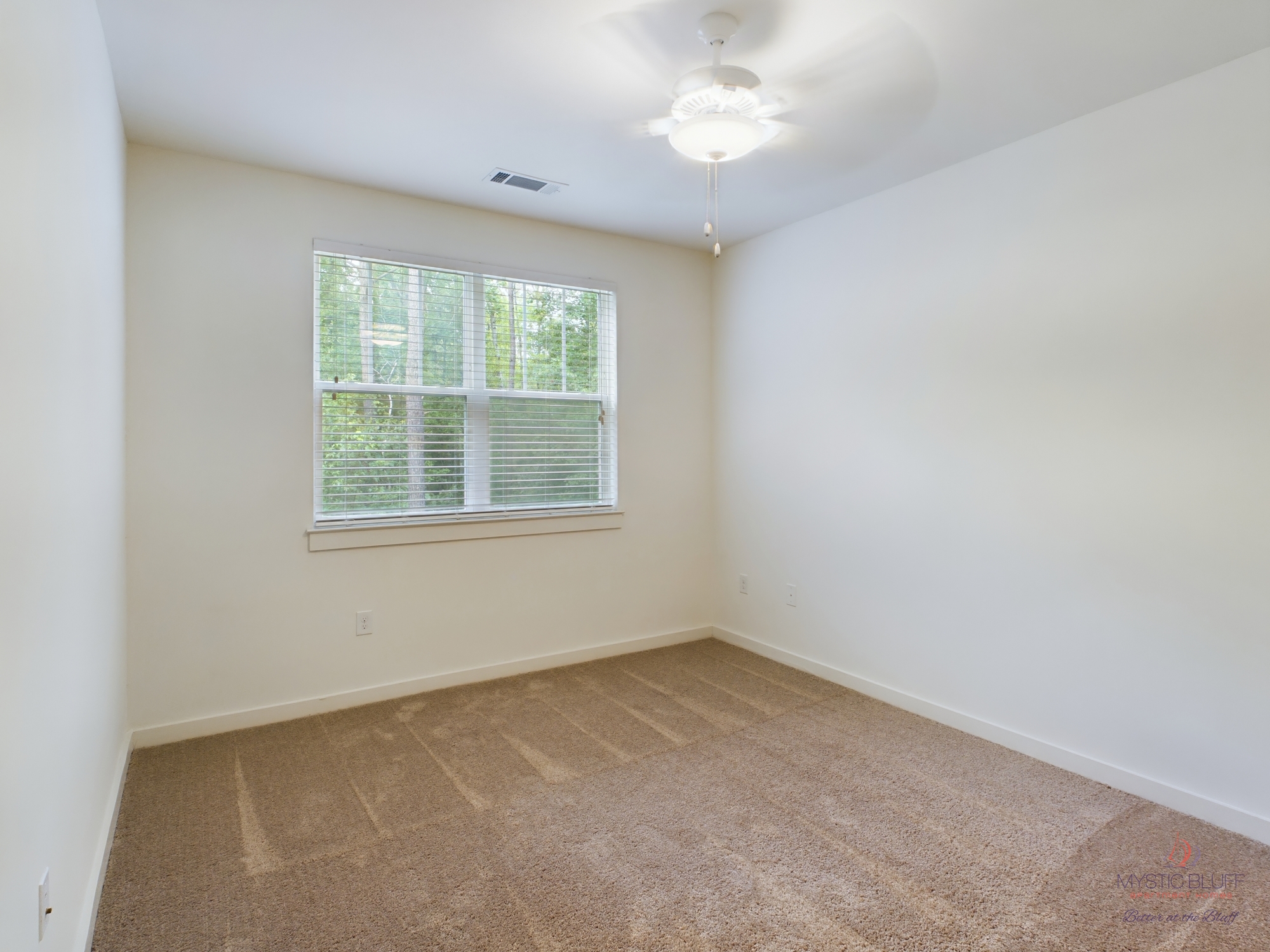 An empty apartment with a ceiling fan and carpet.
