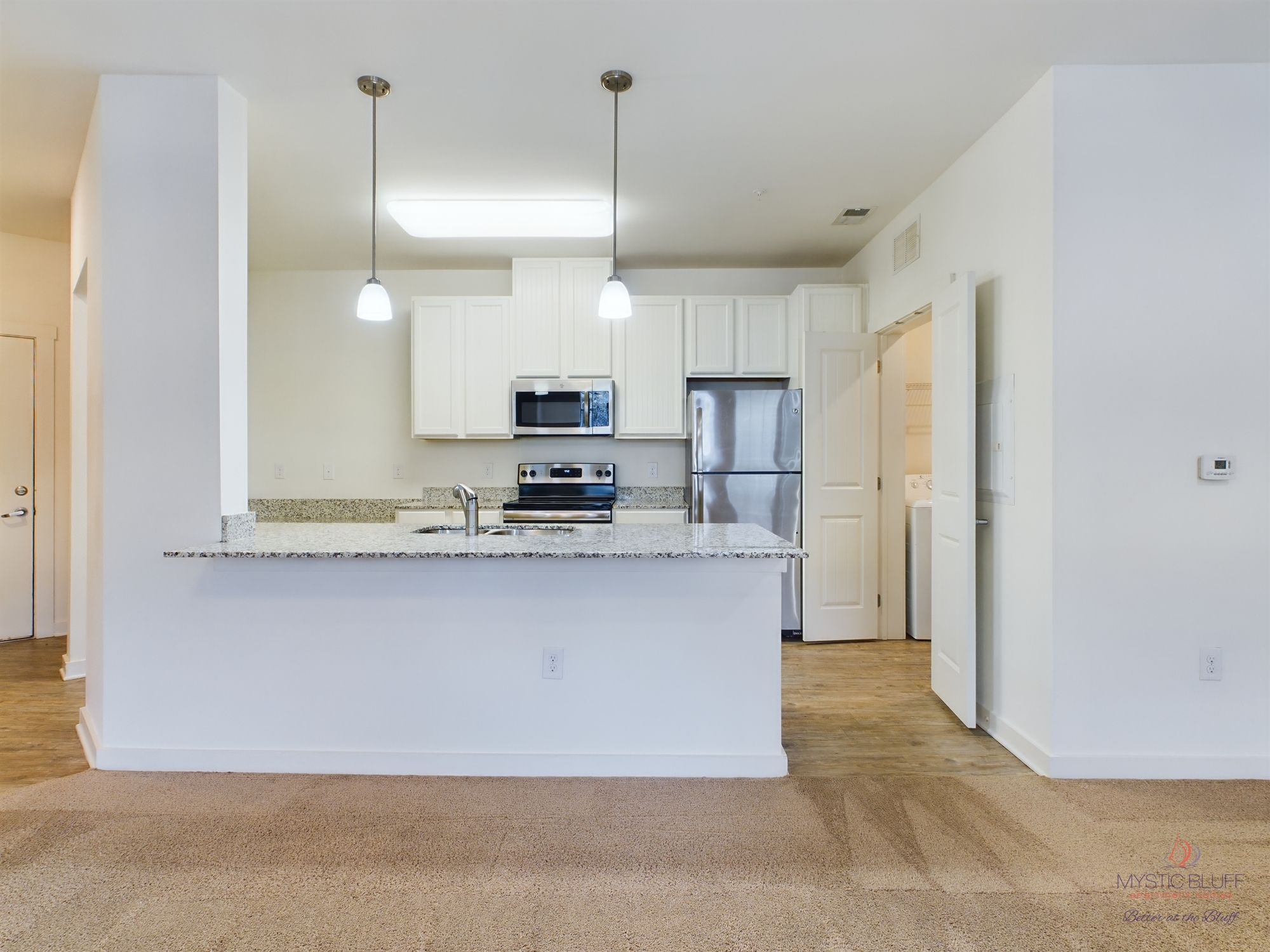 An empty kitchen in apartments with white cabinets and stainless steel appliances.