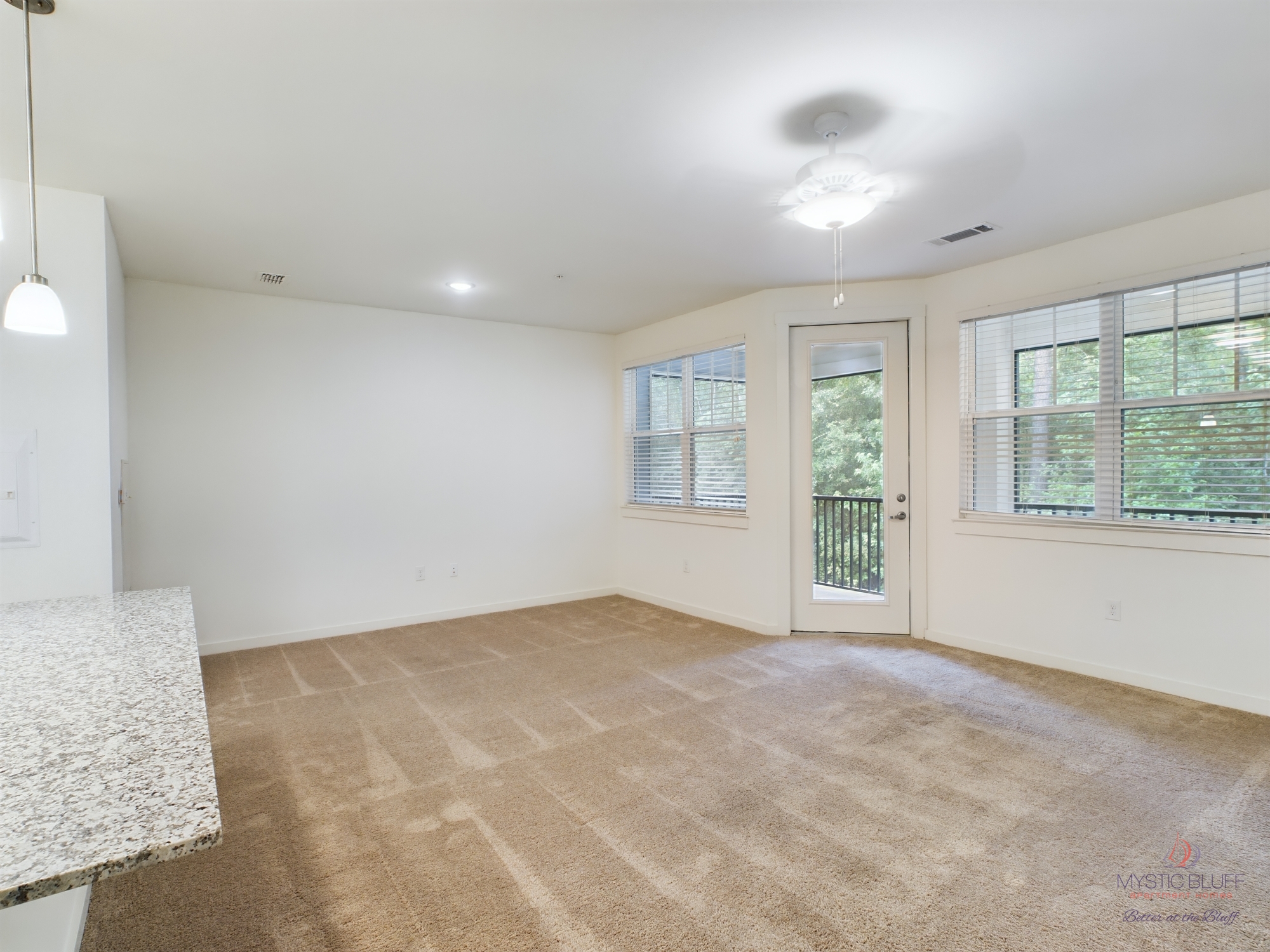 An empty living room in an apartment with a ceiling fan and carpet.