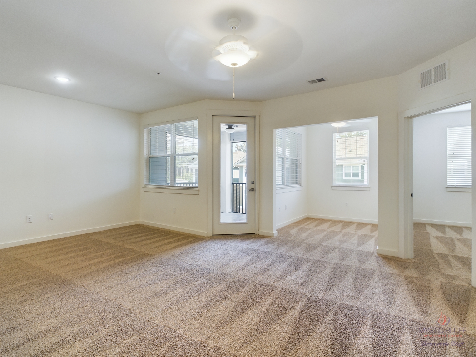 Empty living room with beige carpet and ceiling fan in apartments.