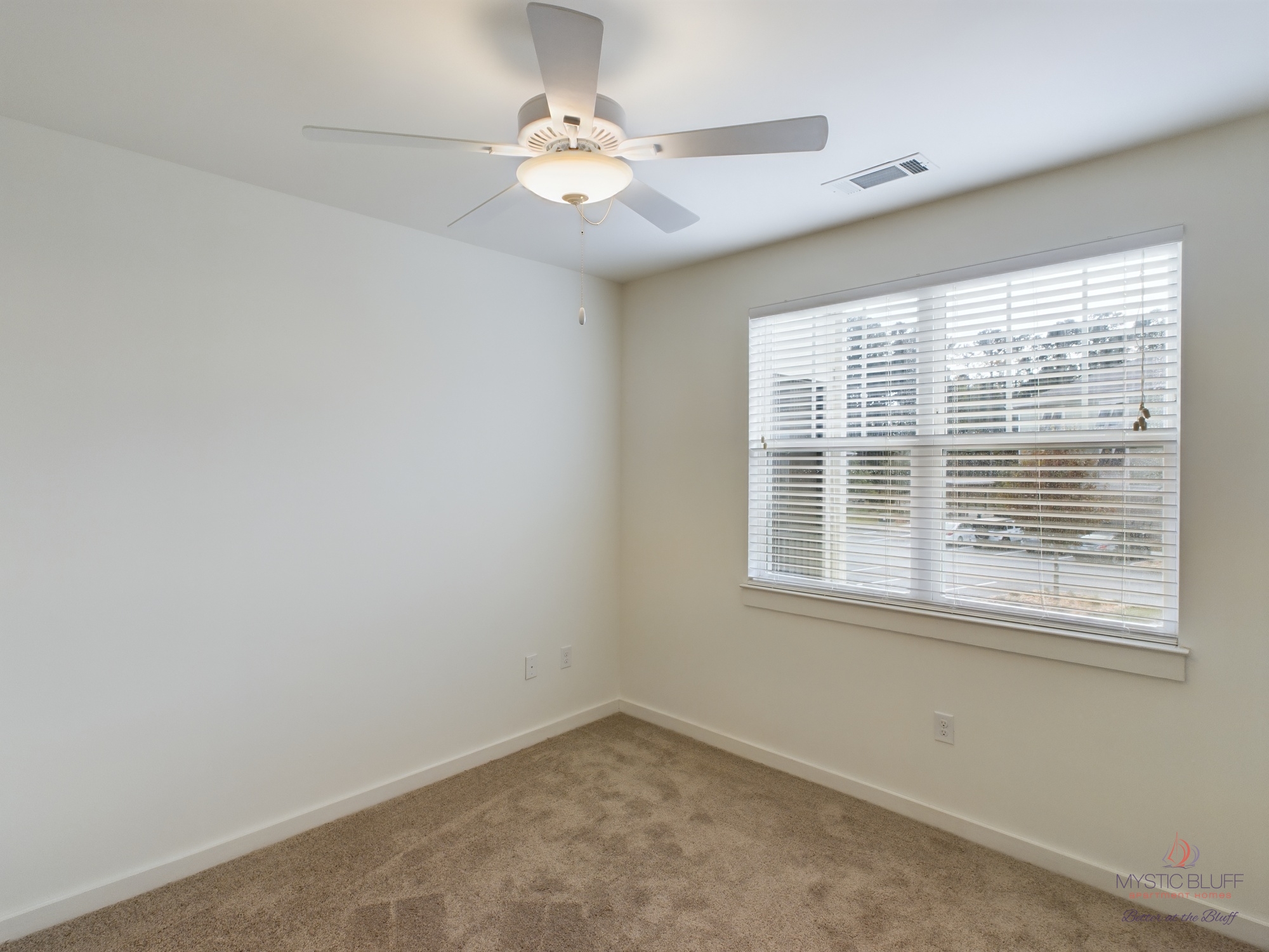 An empty apartment room with a ceiling fan and window.