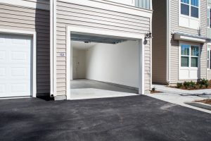 Apartments in Bluffton A clean, empty two-car garage with an open door is attached to a beige-colored house with white trim. The driveway and surrounding pavement are freshly paved.