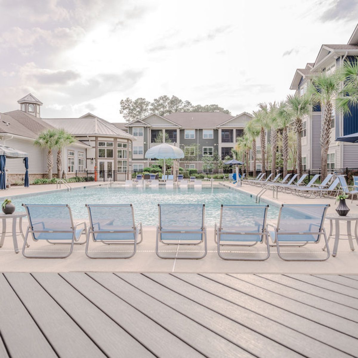 Apartments in Bluffton An outdoor swimming pool at an apartment complex, surrounded by lounge chairs and shaded cabanas, with multi-story buildings in the background.