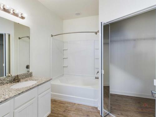 Apartments in Bluffton A bathroom featuring a bathtub-shower combo, a granite countertop vanity with a single sink, a mirror, and a walk-in closet with wooden flooring.