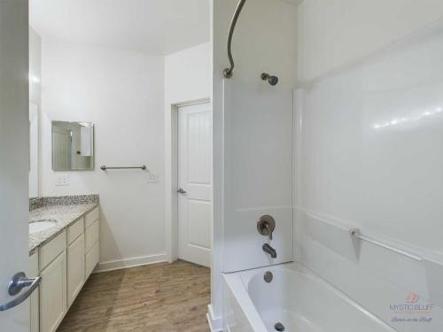 Apartments in Bluffton A bathroom with a bathtub and shower, a granite countertop with sink and mirror, a towel bar mounted on the wall, and a wooden floor.