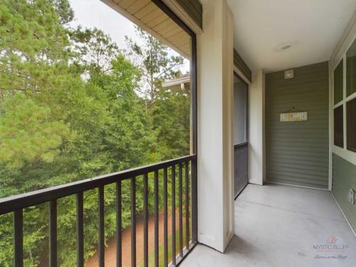 Apartments in Bluffton A covered balcony with beige flooring and a black metal railing overlooks a forested area. The balcony has light green siding and a sign with the word RELAX.