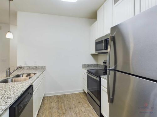 Apartments in Bluffton A kitchen with white cabinets, granite countertops, stainless steel appliances including a refrigerator and microwave, a built-in sink, and a dishwasher. The floor is made of light-colored wood.