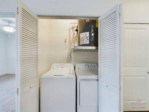 Apartments in Bluffton A laundry area with a washing machine and dryer in an enclosed space with louvered doors; a water heater is mounted above.