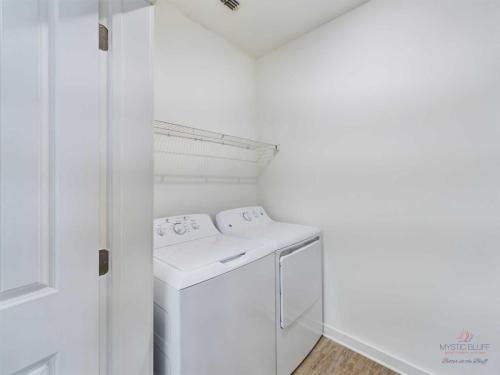 Apartments in Bluffton A laundry room with a washer and dryer set side by side, a wire shelf above them, and white walls.