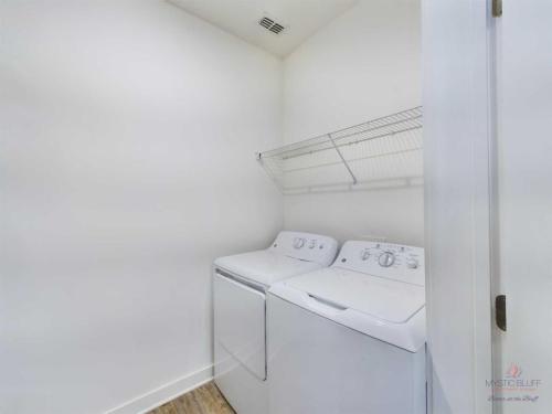 Apartments in Bluffton A laundry room with a white washing machine and dryer, a wire shelf above them, and white walls.