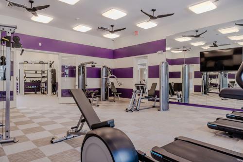 Apartments in Bluffton A modern gym with various exercise equipment including weight machines and treadmills, purple and white walls, large mirrors, and overhead fans. A separate room with additional equipment is visible.