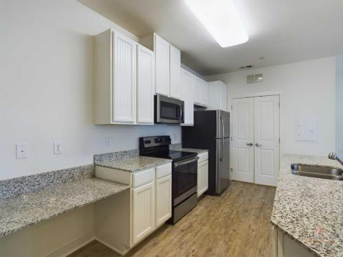 Apartments in Bluffton A modern kitchen featuring stainless steel appliances, granite countertops, white cabinetry, a double sink, and a wood flooring.