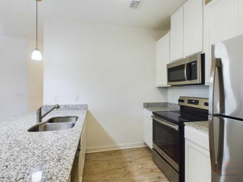 Apartments in Bluffton A modern kitchen with granite countertops, a double sink, stainless steel appliances including a refrigerator, stove, microwave, and white cabinetry. .