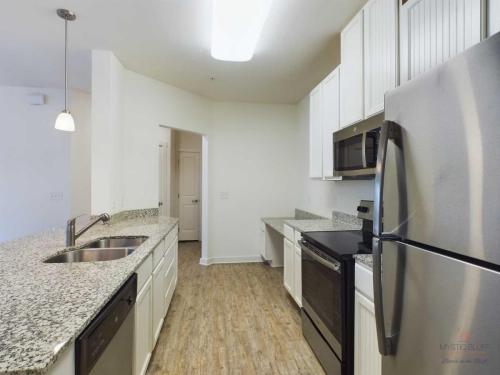 Apartments in Bluffton A modern kitchen with stainless steel appliances, white cabinets, granite countertops, and wooden flooring. A pendant light hangs over the sink area.