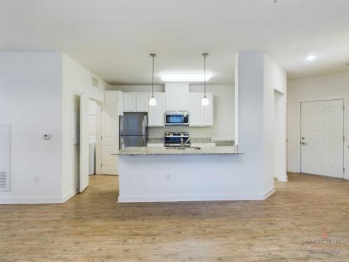 Apartments in Bluffton A modern kitchen with white cabinets, granite countertops, and stainless steel appliances. Two pendant lights hang over a breakfast bar. The room has hardwood floors and white walls.