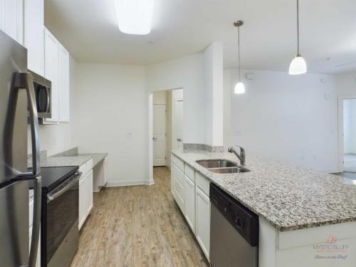 Apartments in Bluffton A modern kitchen with white cabinets, granite countertops, stainless steel appliances, a built-in sink, and a dishwasher. The kitchen features hardwood flooring and overhead lighting.