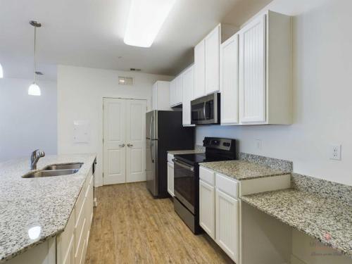 Apartments in Bluffton A modern kitchen with white cabinets, granite countertops, stainless steel appliances, and a wood floor. There is a double-door pantry, a large island with a sink, and overhead lighting.