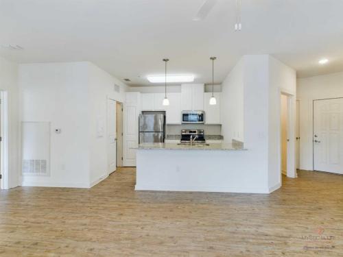 Apartments in Bluffton A modern kitchen with white cabinets, stainless steel appliances, granite countertops, and an island with pendant lighting. The room features wooden flooring and white walls.