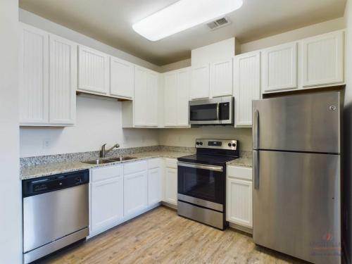 Apartments in Bluffton A modern kitchen with white cabinets, stainless steel appliances including a refrigerator, dishwasher, stove, and microwave, and granite countertops.