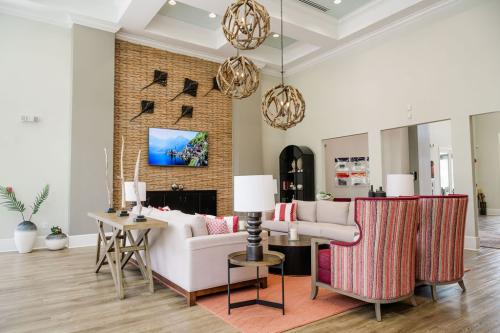 Apartments in Bluffton A modern living room with a U-shaped beige sofa, two red striped chairs, a central coffee table, hanging pendant lights, a wall-mounted TV, and decorative elements like plants and wall art.