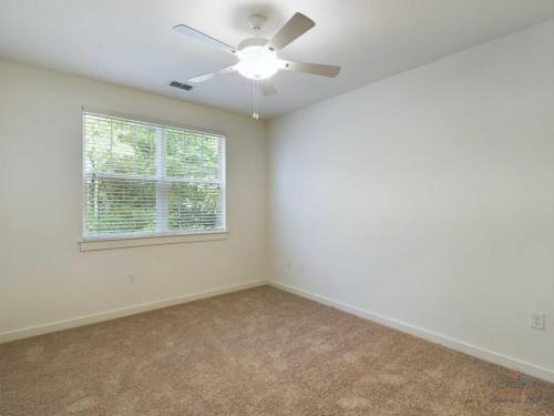 Apartments in Bluffton A room with beige carpet, a white ceiling fan, and a window with white blinds. The walls are painted white.