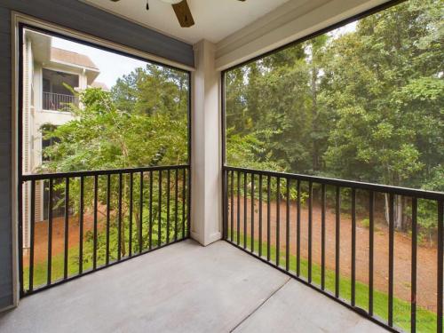 Apartments in Bluffton A screened-in balcony overlooking a wooded area, featuring metal railings and a ceiling fan on a clear day.