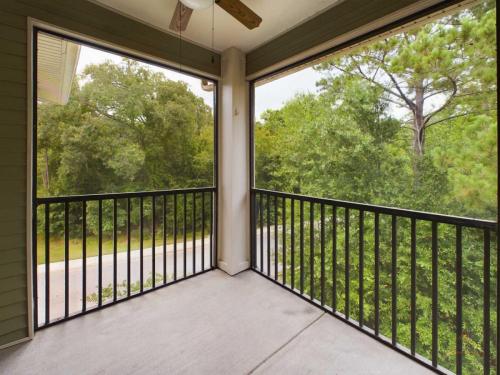 Apartments in Bluffton A screened-in balcony with a view of trees and greenery, featuring a black railing and ceiling fan, overlooking a residential street.