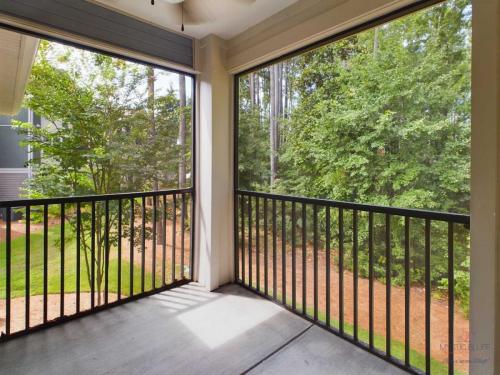 Apartments in Bluffton A screened-in porch with black metal railings overlooking a grassy area lined with tall trees.