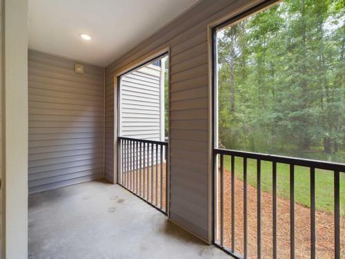 Apartments in Bluffton A screened-in porch with grey siding, black metal railing, and a view of a green yard with trees.