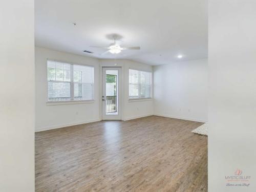 Apartments in Bluffton A well-lit empty room with wood flooring, a ceiling fan, and large windows. A door with glass panes leads outside.