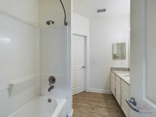 Apartments in Bluffton Bathroom with a bathtub and shower combination, granite countertop with a sink and mirror, white cabinets, and wood flooring.