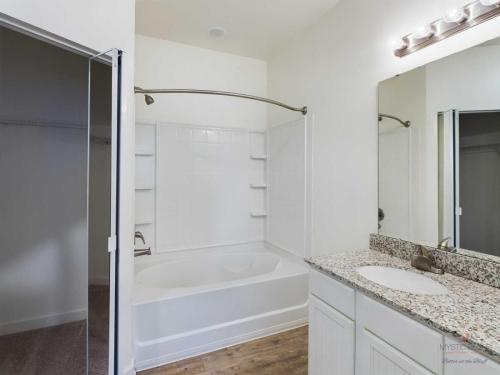 Apartments in Bluffton Bright bathroom with a bathtub-shower combination, a granite countertop with a sink, a large mirror, and wood flooring.