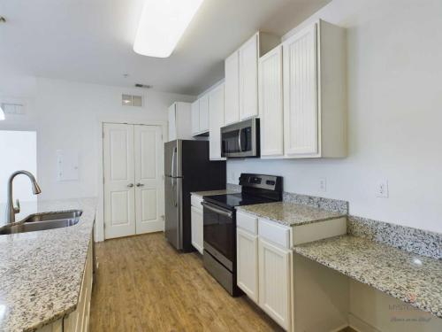 Apartments in Bluffton Bright, modern kitchen with granite countertops, stainless steel appliances, white cabinetry, and a wood-look floor.