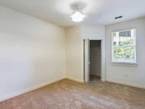 Apartments in Bluffton Empty room with beige carpet, white walls, ceiling fan with light, single window, and open closet door.