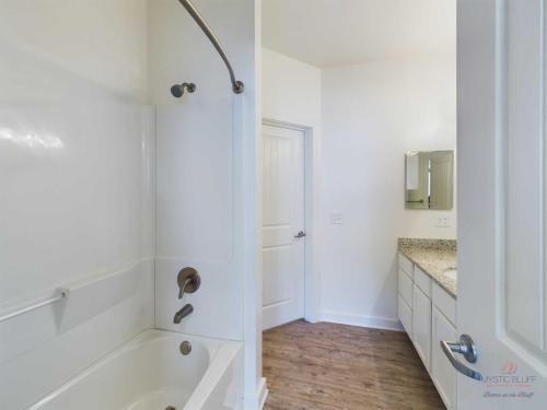 Apartments in Bluffton Modern bathroom with a bathtub-shower combination, a vanity with cabinets and a large mirror, white walls, and wood-look flooring.