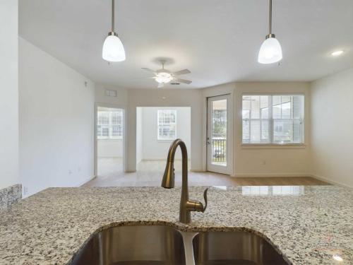 Apartments in Bluffton Modern, bright kitchen with granite countertops, a double sink, pendant lighting, and an open layout leading to a well-lit living area with large windows and a ceiling fan.