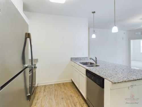 Apartments in Bluffton Modern kitchen featuring stainless steel appliances, a granite countertop island with a sink, and light wood flooring, within a spacious white interior.