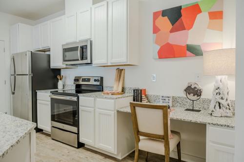 Apartments in Bluffton Modern kitchen interior with white cabinets, stainless steel appliances, granite countertops, and a colorful abstract painting. A small desk with a chair and lamp is placed against the right wall.