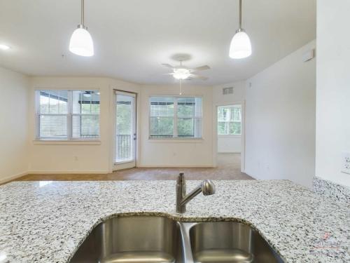 Apartments in Bluffton Modern kitchen sink with granite countertop overlooking an open living area with large windows, ceiling fan, and an adjacent room.