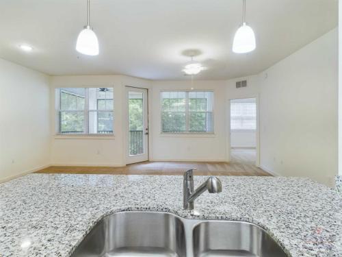 Apartments in Bluffton Modern kitchen view with granite countertops, stainless steel sink, and open layout into a bright living area. Multiple large windows provide ample natural light.