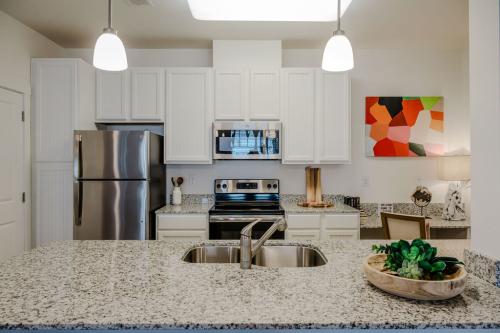 Apartments in Bluffton Modern kitchen with granite countertops, stainless steel appliances, white cabinets, a double sink, and a colorful abstract painting on the wall.