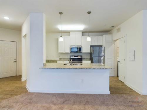 Apartments in Bluffton Modern kitchen with stainless steel appliances, granite countertops, white cabinets, and a breakfast bar. There is hardwood flooring in the kitchen area and carpet in the adjacent area.