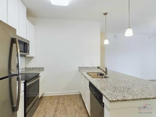 Apartments in Bluffton Modern kitchen with stainless steel appliances, granite countertops, white cabinets, and hardwood floor. Kitchen island includes a sink and dishwasher, and pendant lights hang from the ceiling.