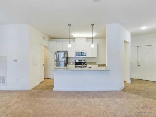 Apartments in Bluffton Modern kitchen with stainless steel appliances, white cabinets, granite countertops, and pendant lights located in an apartment with beige carpeted living area and tile flooring near the entrance.