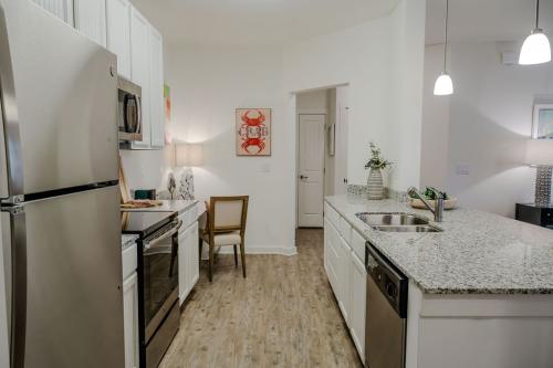 Apartments in Bluffton Modern kitchen with stainless steel appliances, white cabinets, granite countertops, and wooden flooring. Decor includes a crab painting, a chair, and pendant lights over the island.