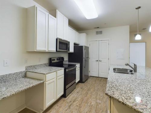 Apartments in Bluffton Modern kitchen with white cabinets, granite countertops, stainless steel appliances, including a microwave and oven, and wood flooring. The room features a double sink and recessed lighting.